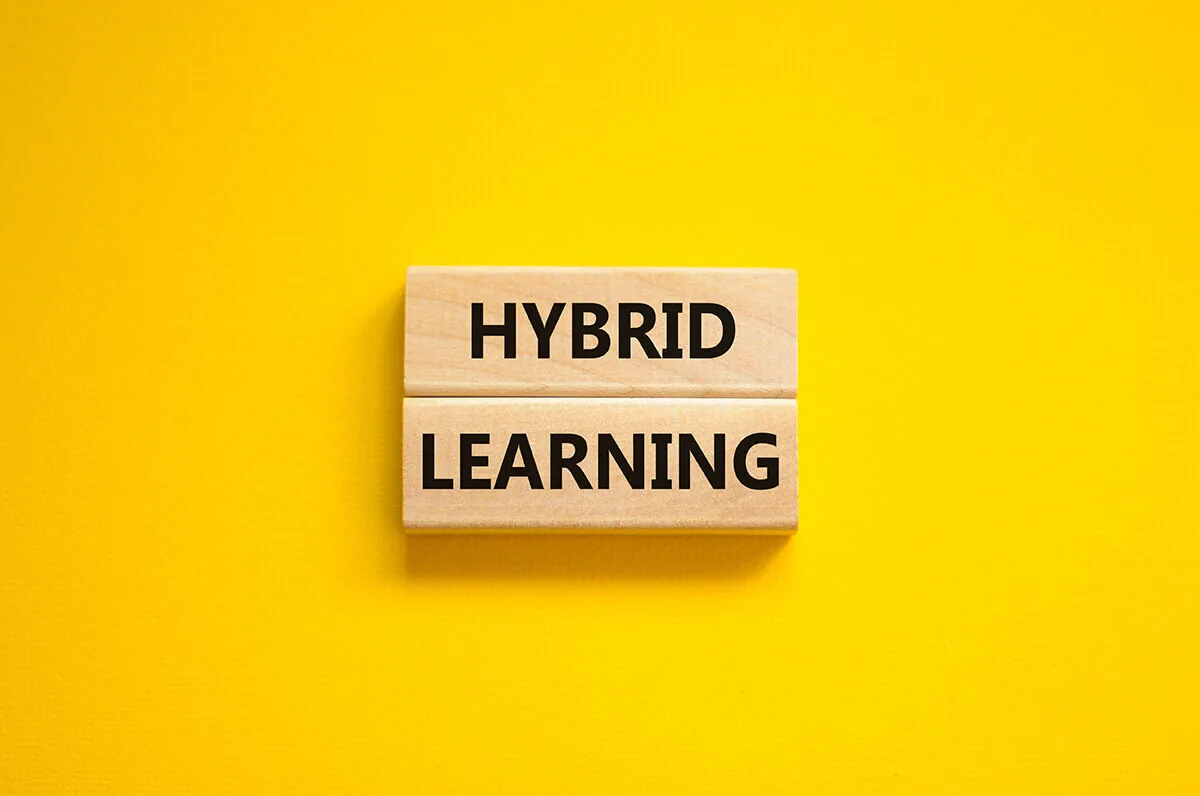 Due blocchi di legno con la scritta hybrid learning su sfondo giallo rappresentano il concetto di apprendimento ibrido