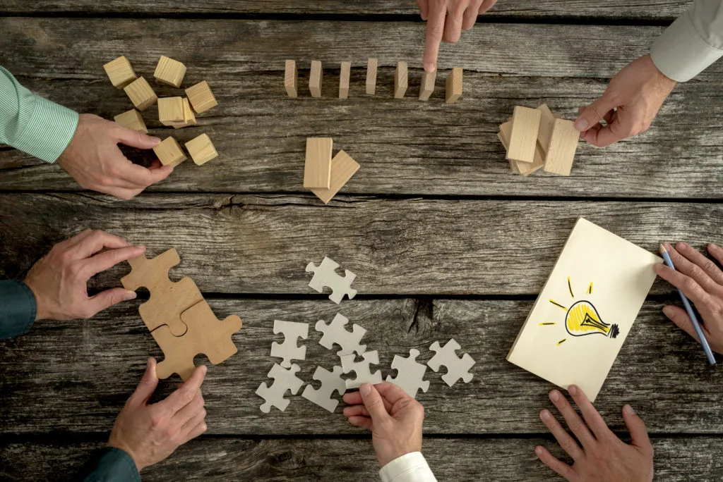 Mani che collaborano con blocchi di legno, puzzle e foglio con lampadina, simbolo di attenzione e problem solving