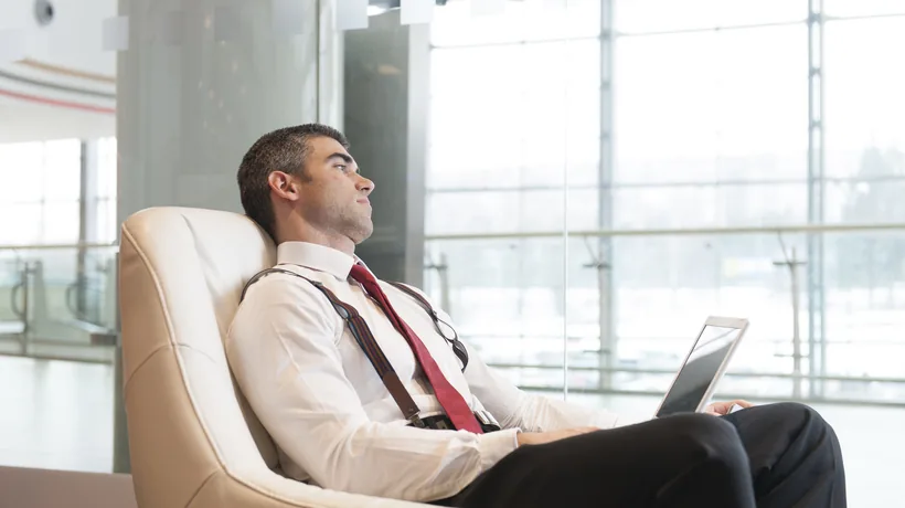 Uomo in abito seduto su una poltrona in ufficio con laptop sulle gambe che appare distratto o annoiato
