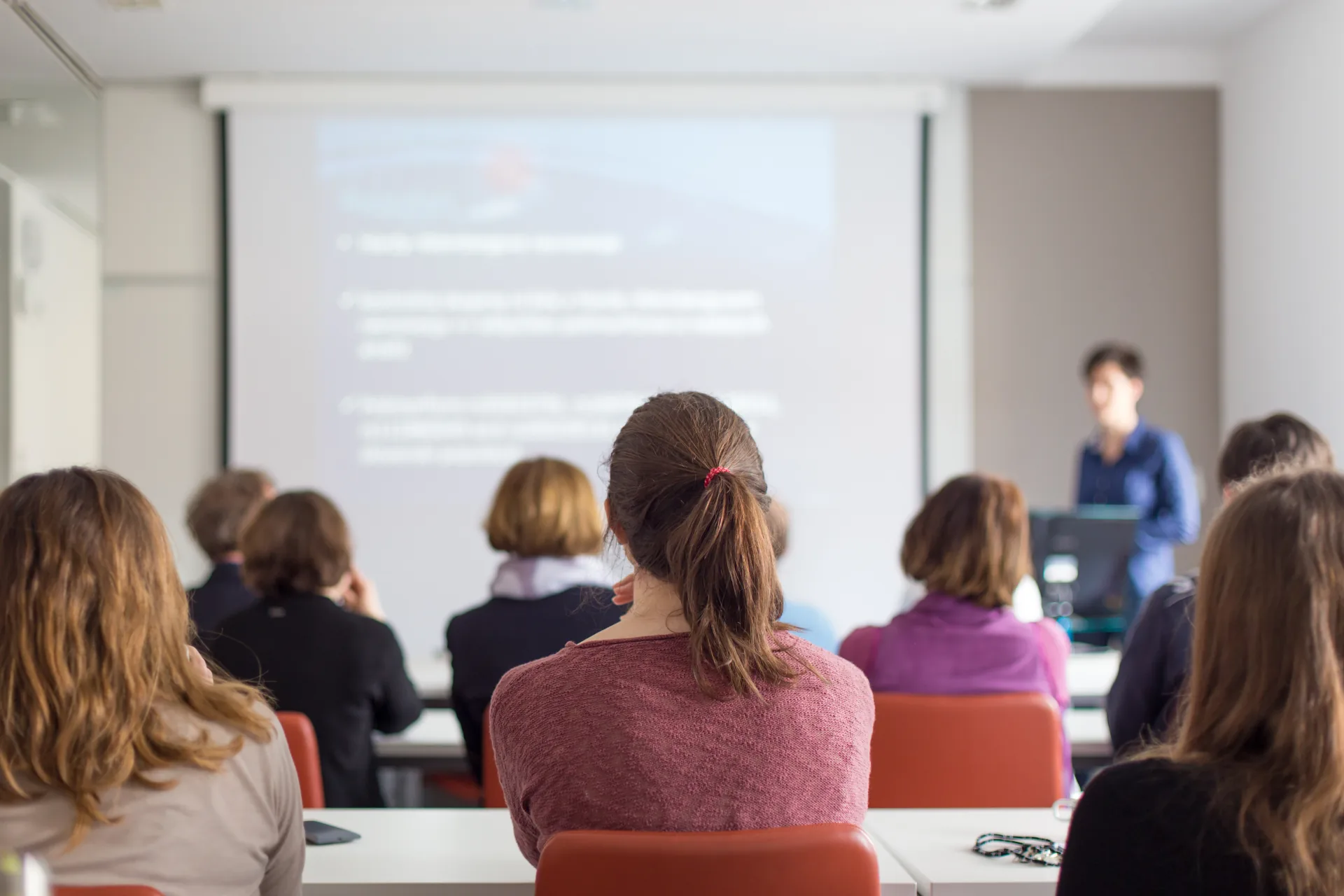 Partecipanti seduti in aula ascoltano un formatore davanti a una presentazione proiettata, esempio di formazione formale