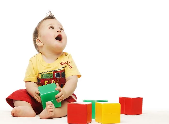 Bambino seduto che osserva con curiosità alcuni cubi colorati, simbolo di apprendimento naturale