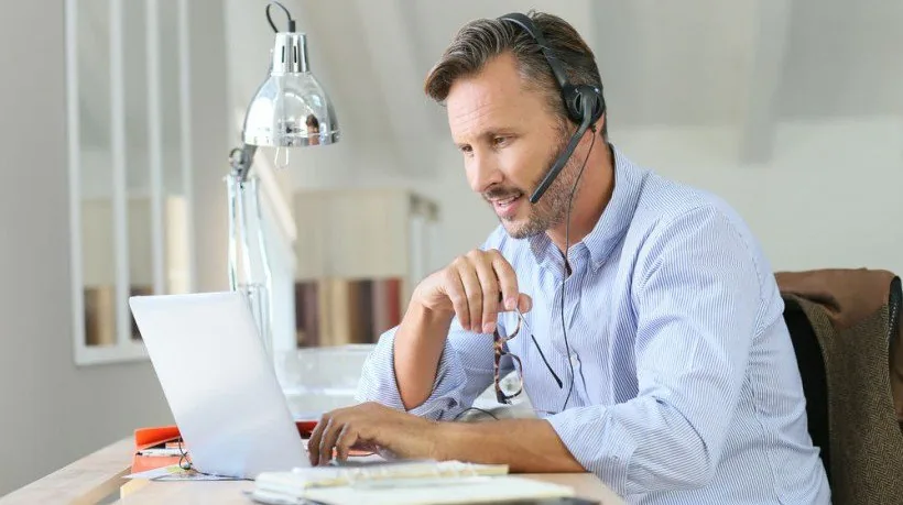Docente con cuffie e microfono interagisce online tramite laptop in un contesto di formazione digitale