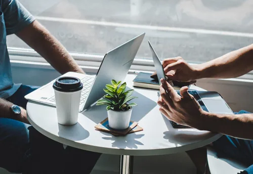 Due persone lavorano insieme a un tavolo con laptop, tablet, smartphone e caffè, simbolo di collaborazione digitale
