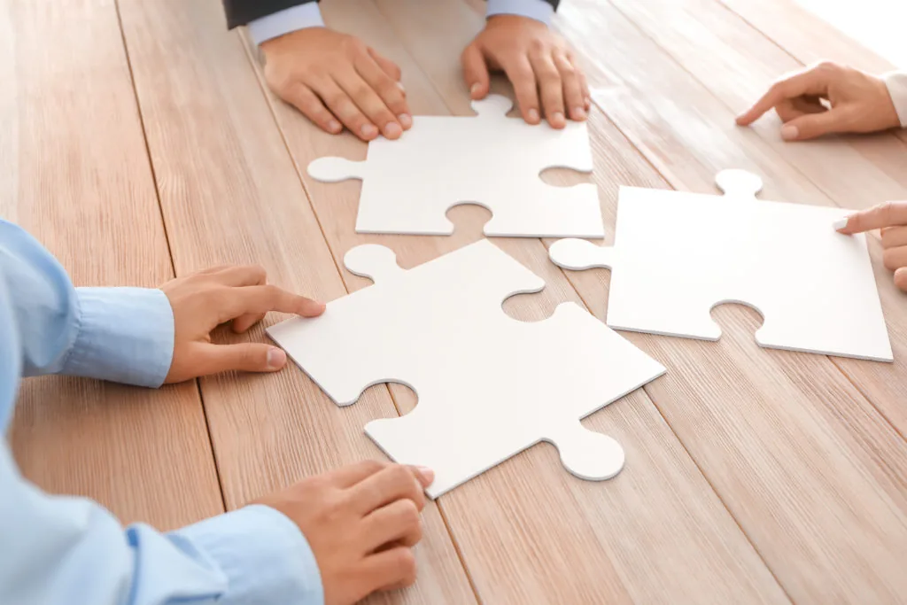 Quattro mani uniscono grandi pezzi di puzzle su un tavolo, simbolo di collaborazione nella creazione di corsi elearning