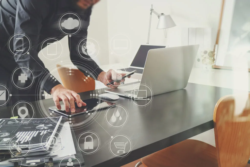 Persona lavora su laptop, tablet e smartphone con icone digitali che rappresentano interazione e tecnologia nell’e-learning