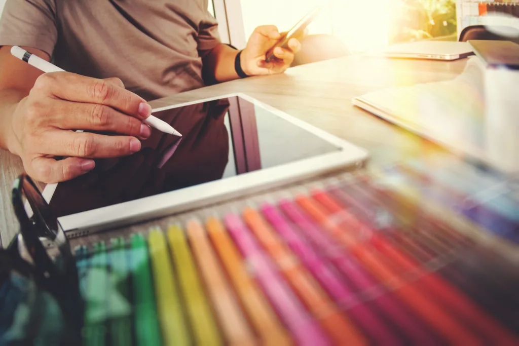 Persona utilizza uno stilo su tablet con colori e smartphone su scrivania, simbolo di creatività digitale per presentazioni