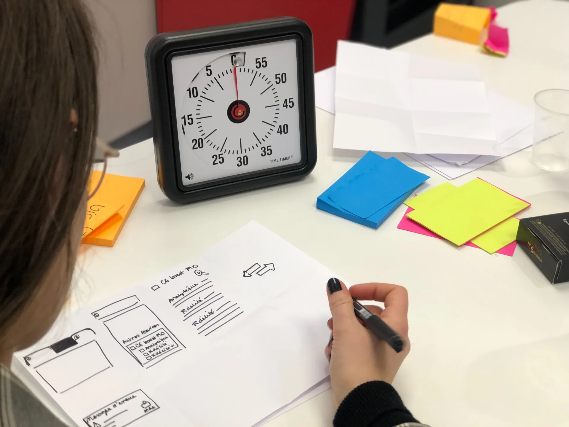 Persona disegna un prototipo su carta con timer e post-it colorati durante una sessione di Design Thinking