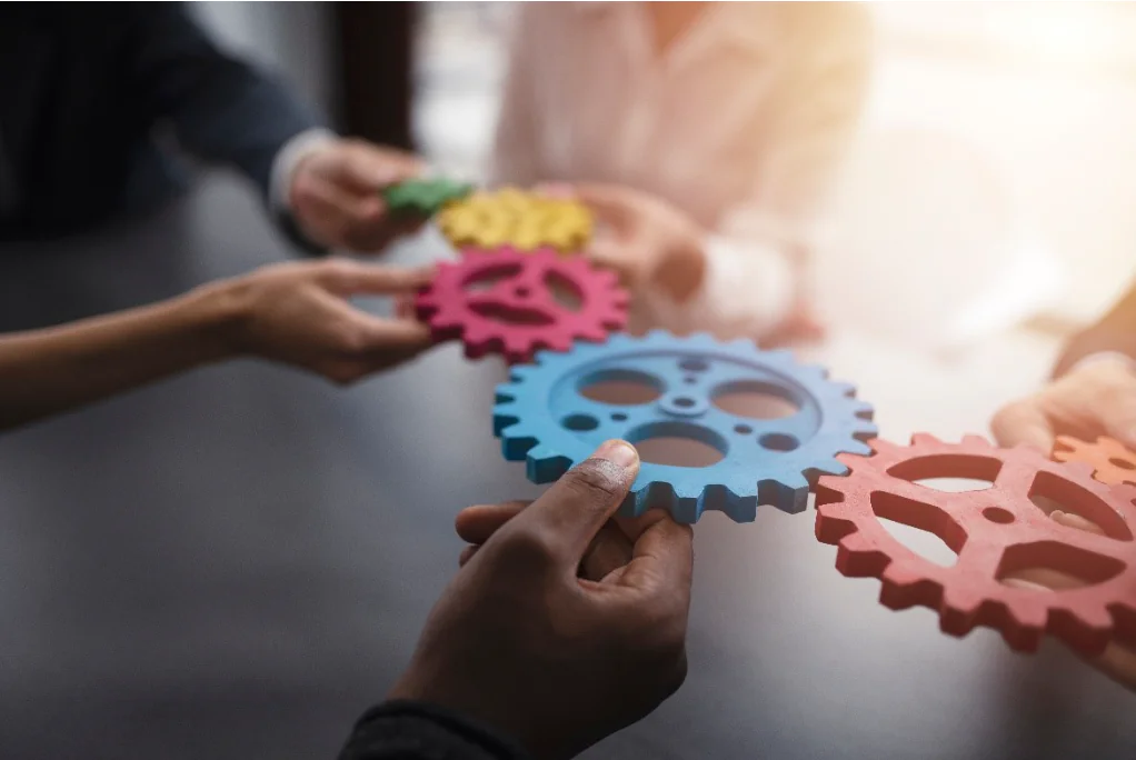Mani di persone diverse che uniscono ingranaggi colorati a simboleggiare collaborazione e inclusione sul lavoro