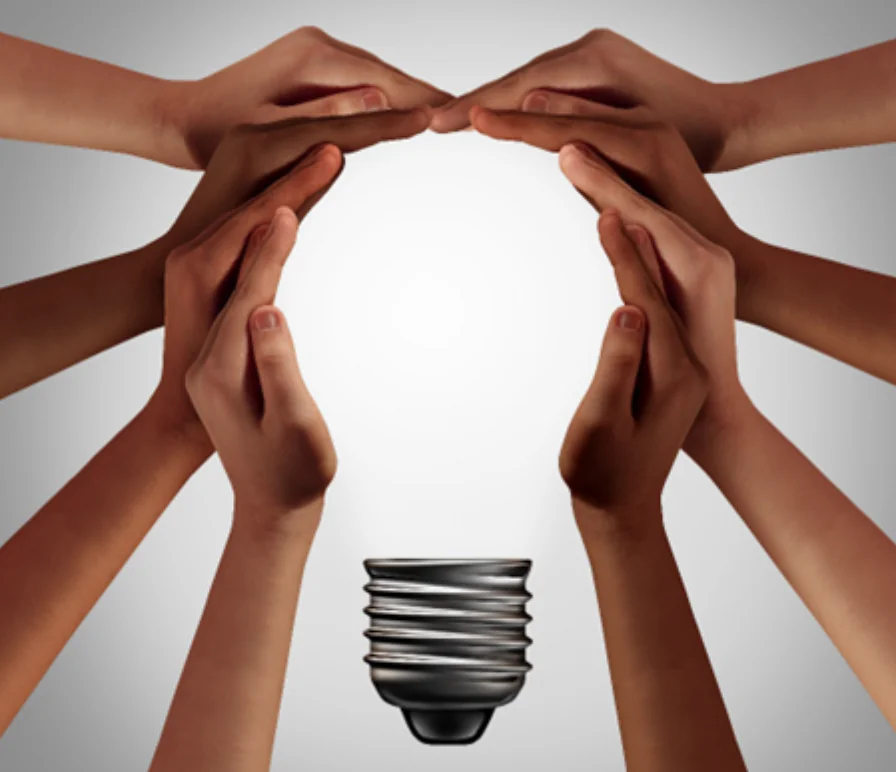 Mani di persone diverse formano la sagoma di una lampadina, simbolo di collaborazione e inclusione nel lavoro