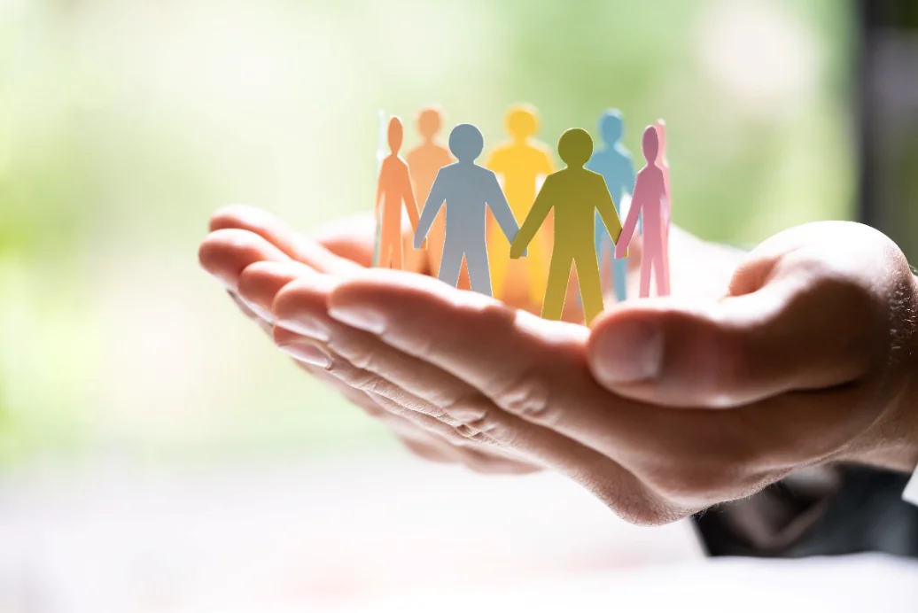 Mani che sorreggono sagome di persone colorate simbolo di diversità e inclusione nel contesto lavorativo