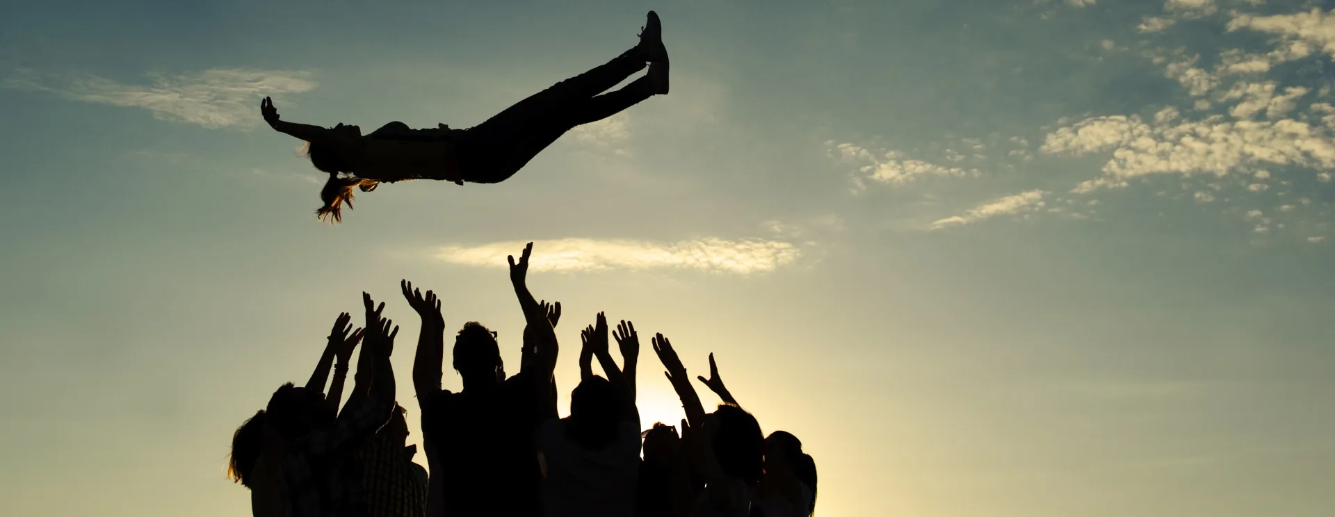 Un gruppo di persone solleva in aria un membro del team al tramonto, simbolo di fiducia e collaborazione
