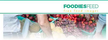 Due persone raccolgono frutta fresca da cassette colorate, con il logo FoodiesFeed in alto