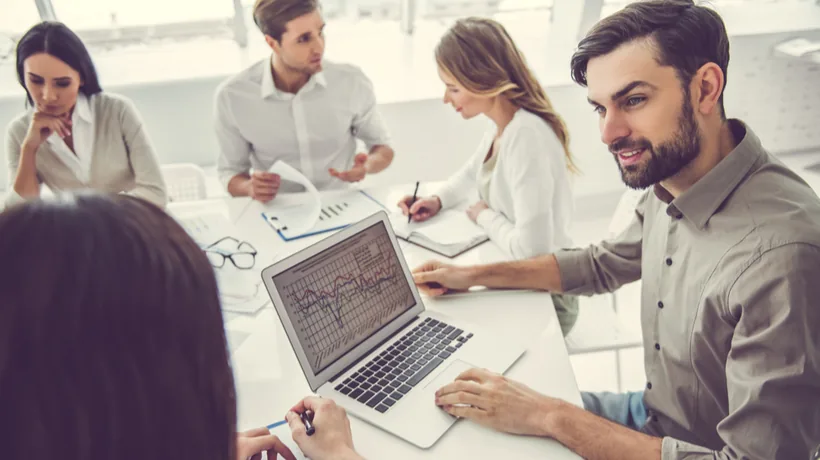 Gruppo di persone in ufficio discute davanti a un laptop con grafico, rappresentando formazione digitale sul prodotto