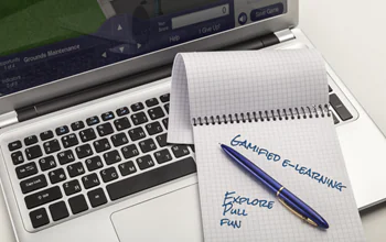 Blocco note con scritta gamified e-learning e penna appoggiati su un laptop acceso con corso digitale