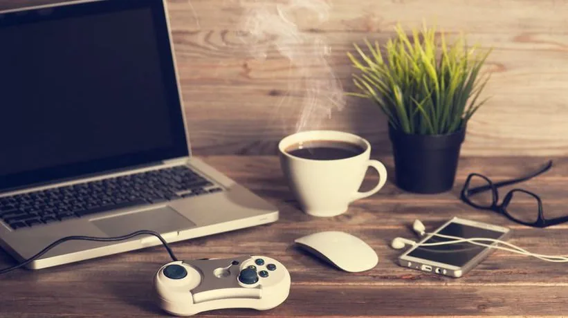 Scrivania con laptop, controller da gioco, caffè e smartphone che simboleggiano la gamification in ambito aziendale