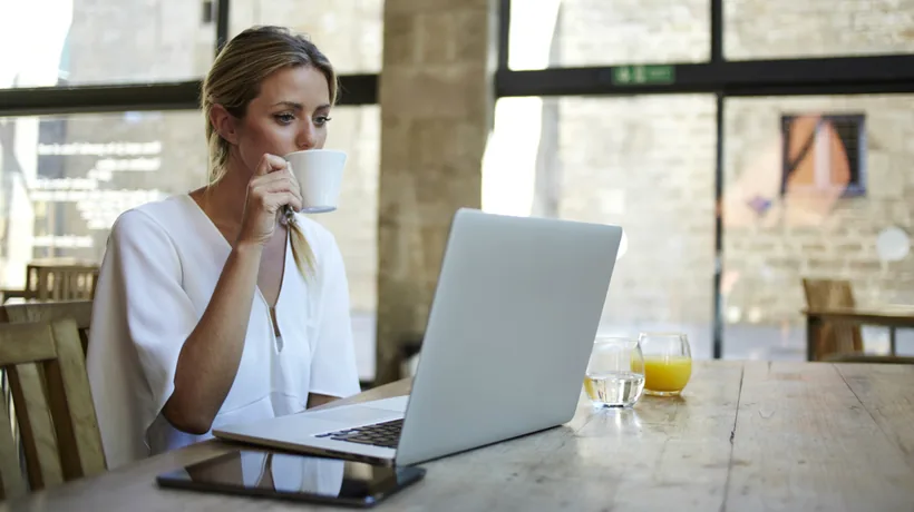 Donna lavora al computer portatile in un ambiente luminoso mentre beve una bevanda, simbolo di gestione del tempo online