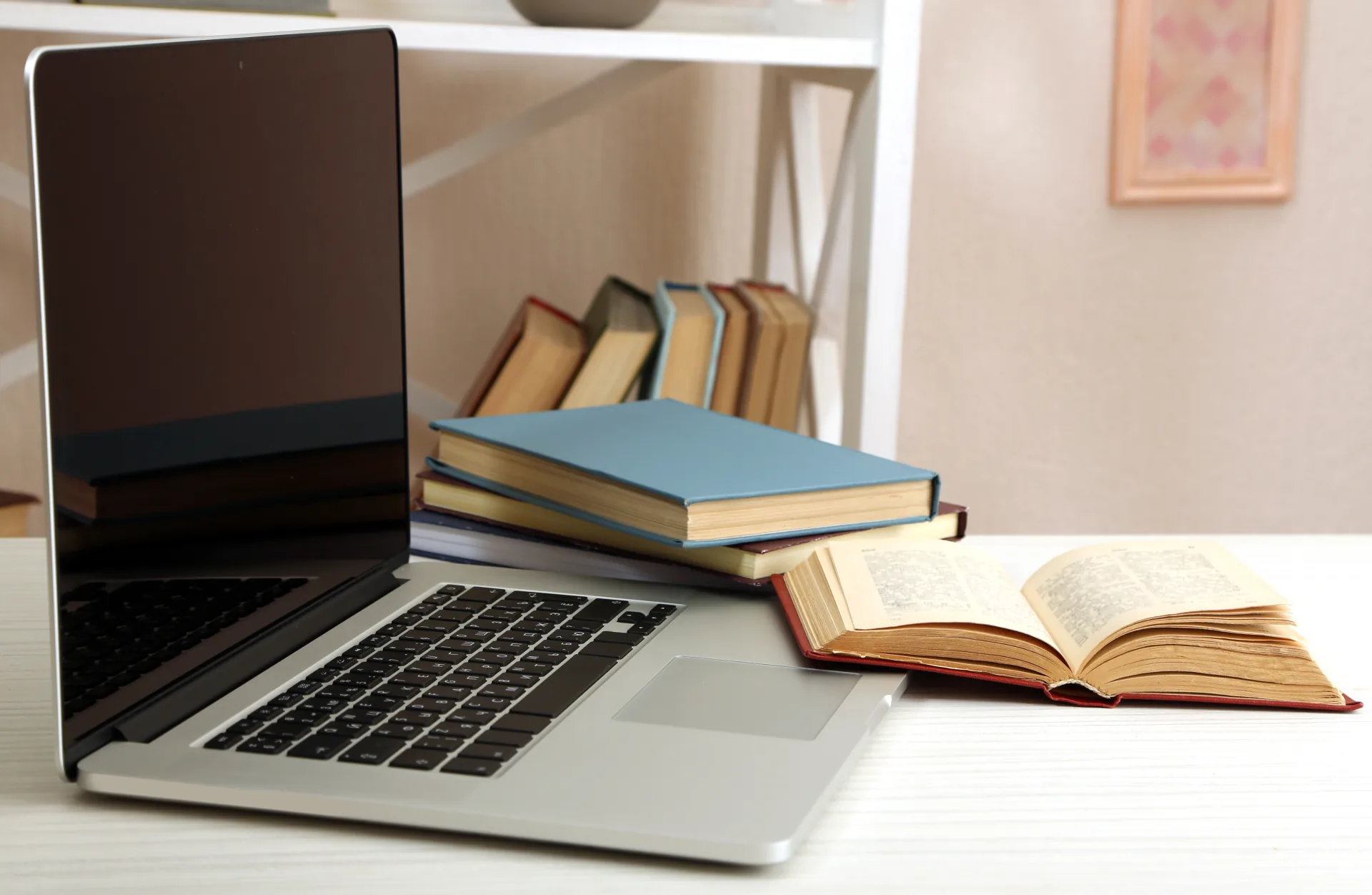 Computer portatile su scrivania con libri chiusi e un libro aperto, simbolo di apprendimento digitale e tradizionale