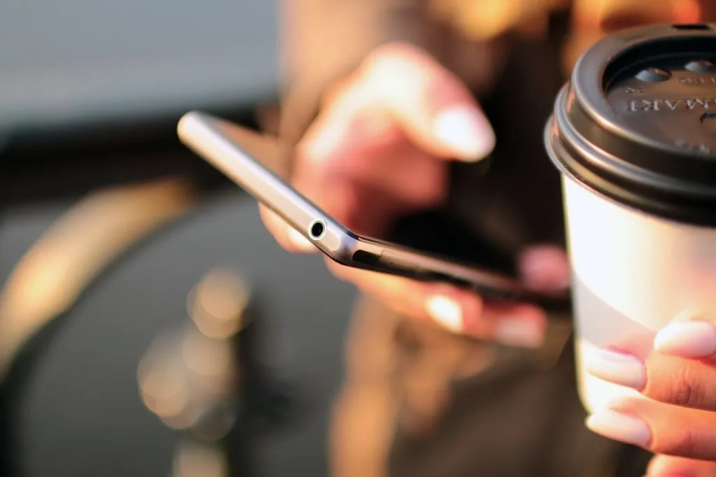 Persona tiene uno smartphone e una tazza da asporto, rappresentando l'apprendimento digitale pratico e accessibile ovunque