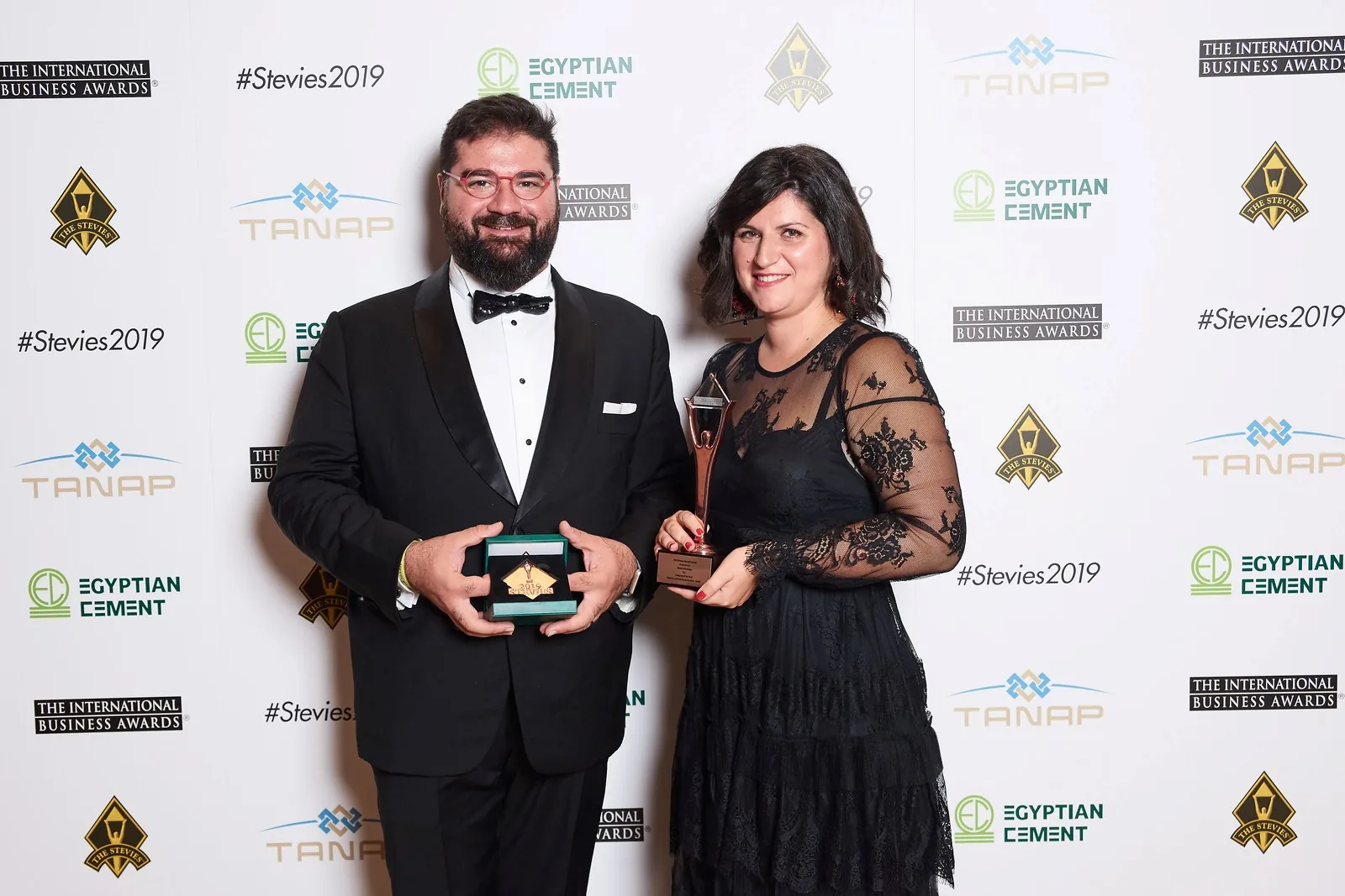 Due persone eleganti posano sorridenti con i trofei ricevuti agli International Business Awards 2019