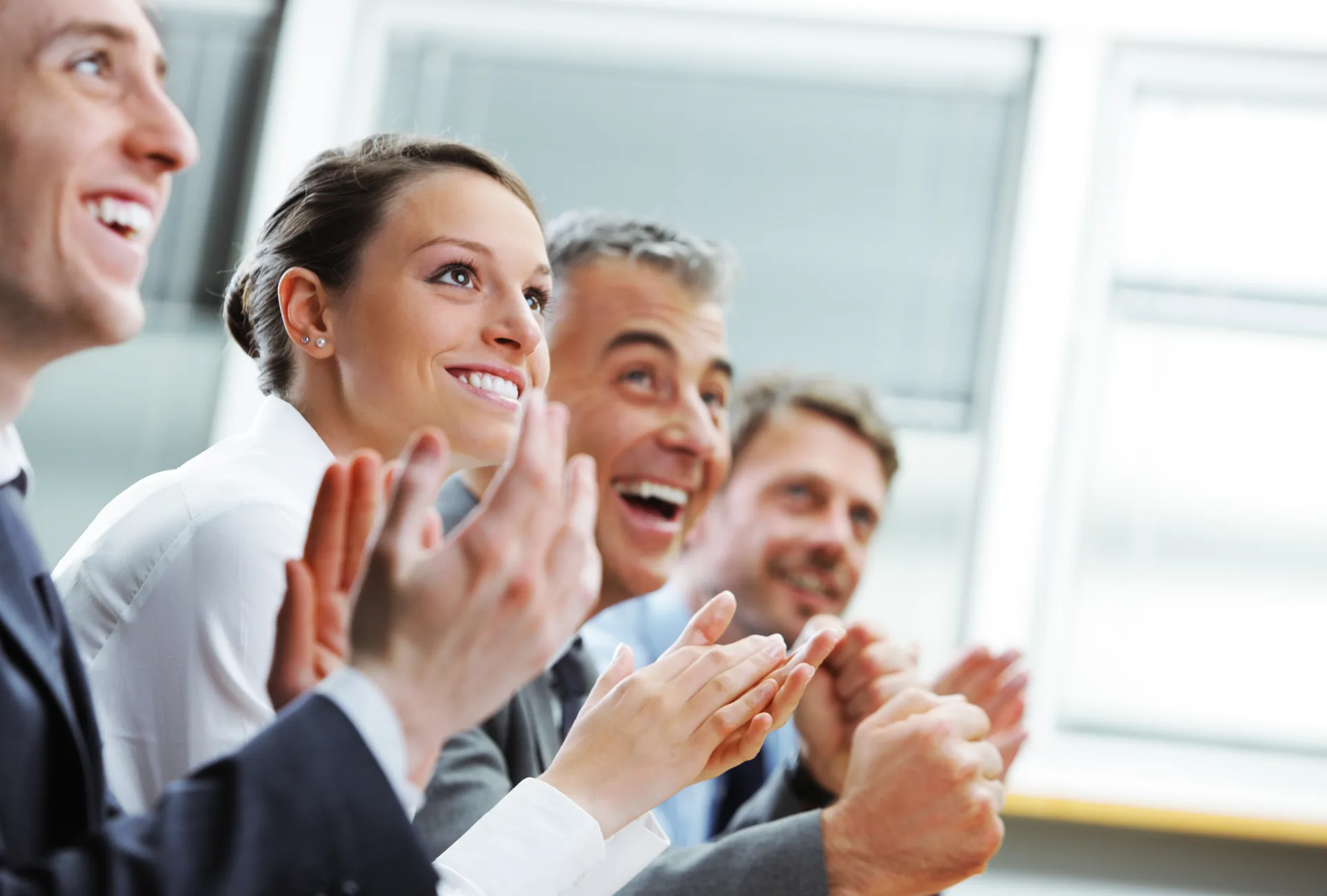 Gruppo di colleghi in abbigliamento formale che applaude con entusiasmo durante un momento di riconoscimento lavorativo