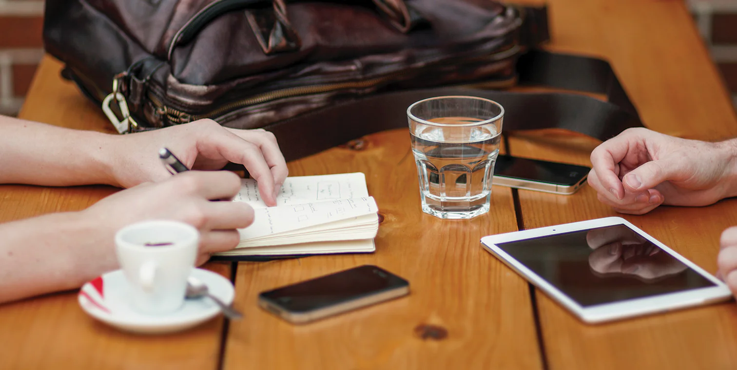 Due persone discutono e prendono appunti con tablet e smartphone su un tavolo durante una sessione di lavoro