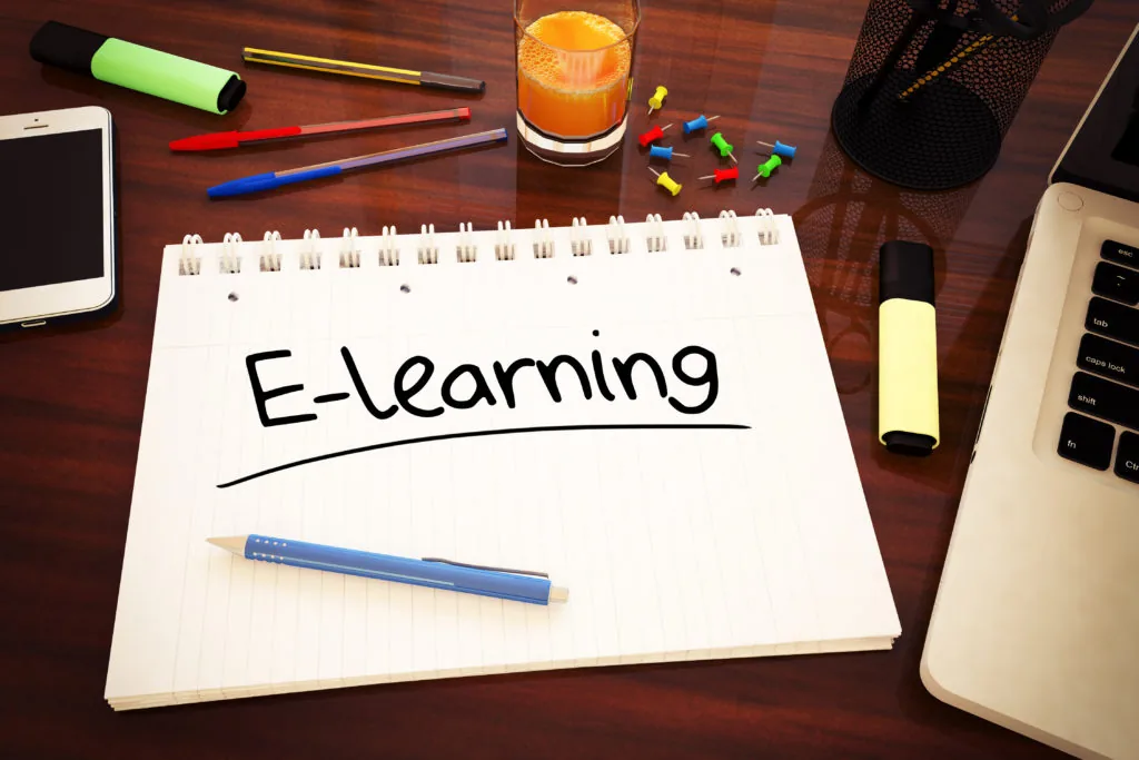 Quaderno a spirale con la scritta E-learning su una scrivania con laptop, penne e accessori digitali