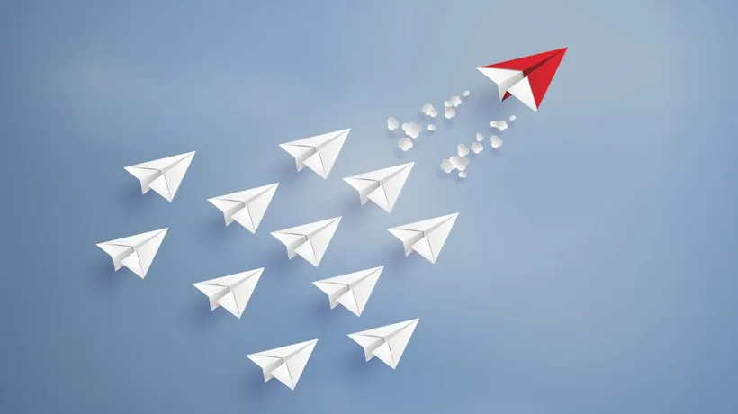 Un gruppo di aerei di carta bianchi segue un aereo di carta rosso che vola davanti, simbolo di leadership e guida