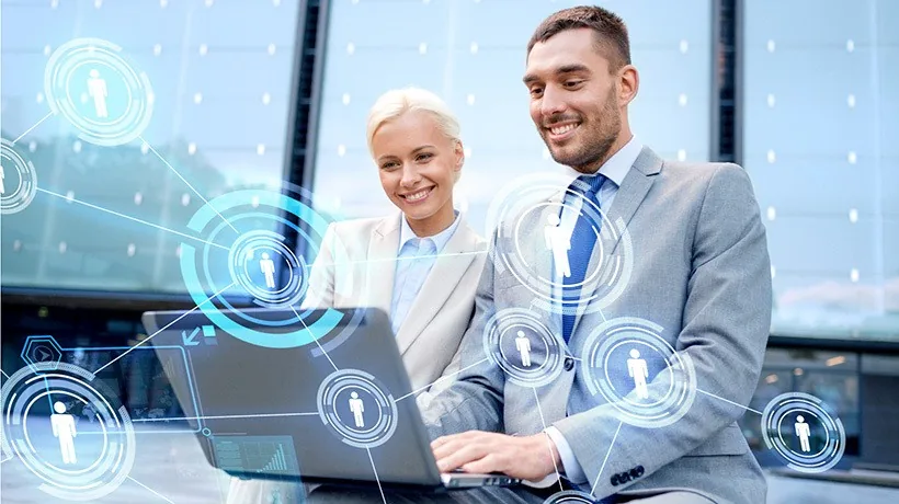 Due professionisti collaborano online su un laptop con icone digitali che rappresentano connessioni sociali