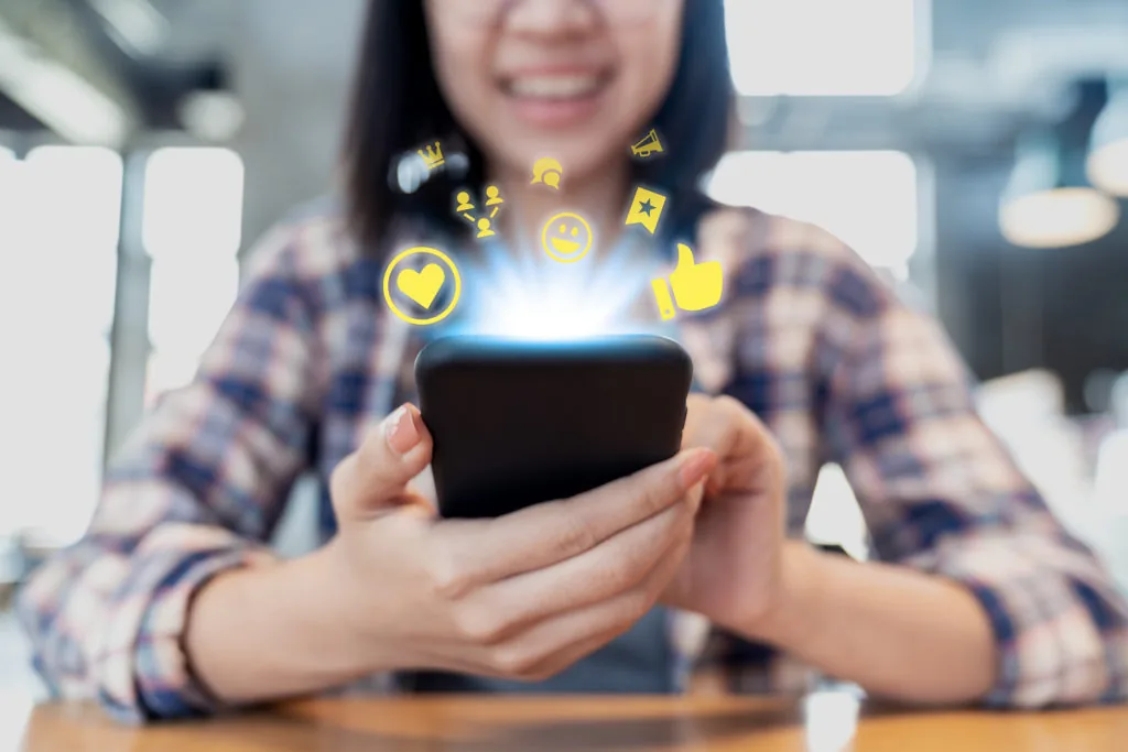 Persona che sorride mentre usa uno smartphone con icone social che simboleggiano interazione e collaborazione digitale
