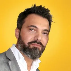 Ritratto di un uomo con barba e capelli scuri su sfondo giallo, speaker di LEARNING 360 su storytelling e Articulate 360