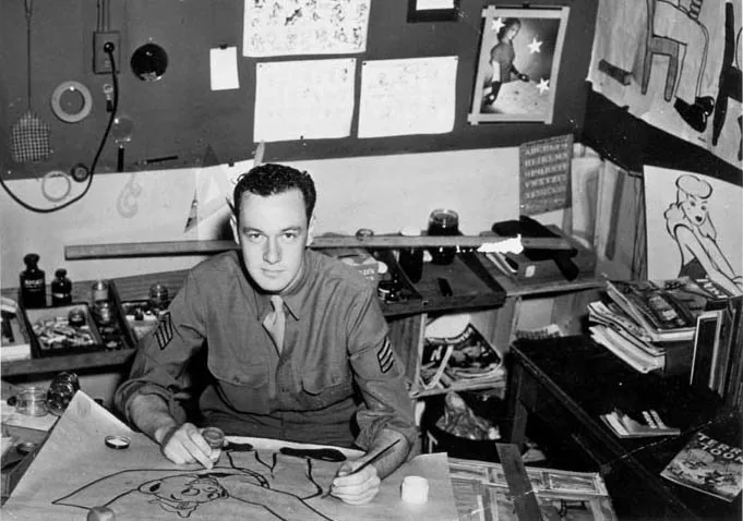 Un giovane in uniforme militare disegna su un grande foglio circondato da materiali illustrativi e fumetti