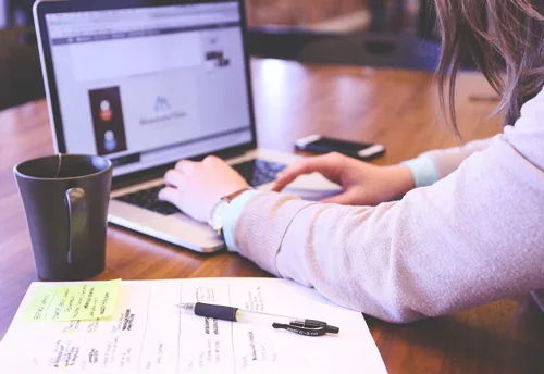 Persona utilizza un computer portatile per attività di e-learning con appunti e tazza su un tavolo