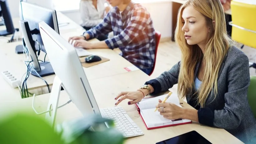 Studentessa utilizza computer e prende appunti su un quaderno durante una sessione di e-learning in un ambiente collaborativo