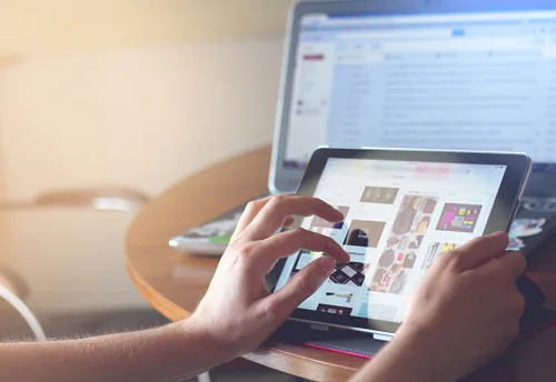 Persona utilizza un tablet per consultare contenuti digitali e-learning con un laptop sullo sfondo