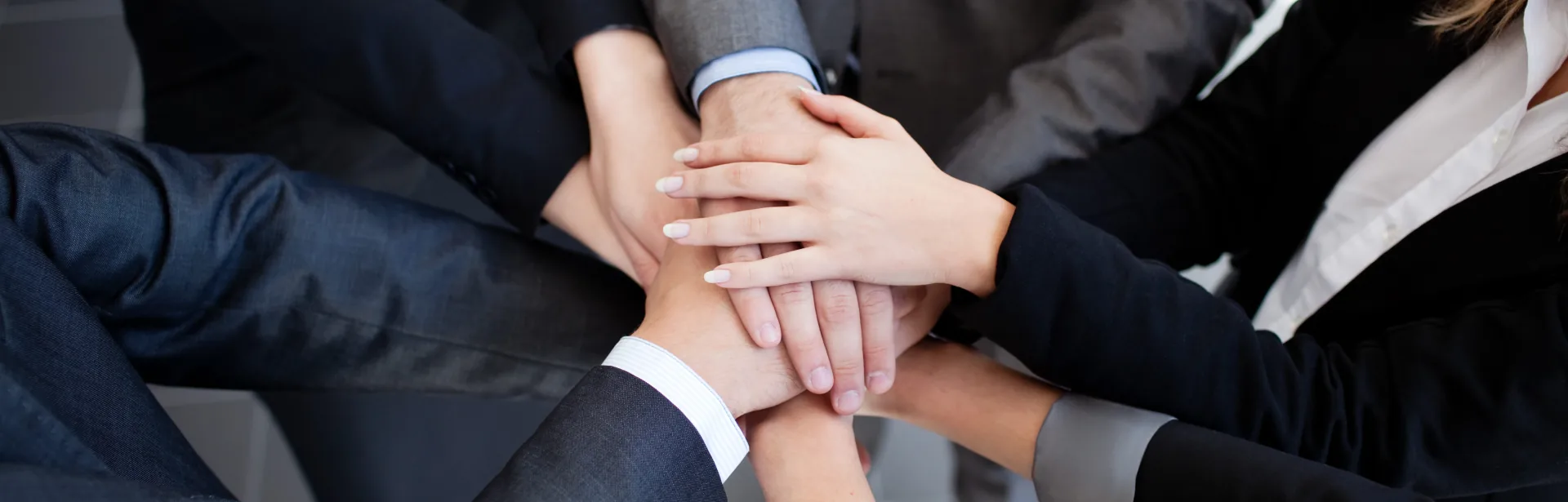 Mani di persone in abiti formali sovrapposte che rappresentano collaborazione e team-building nella formazione manageriale