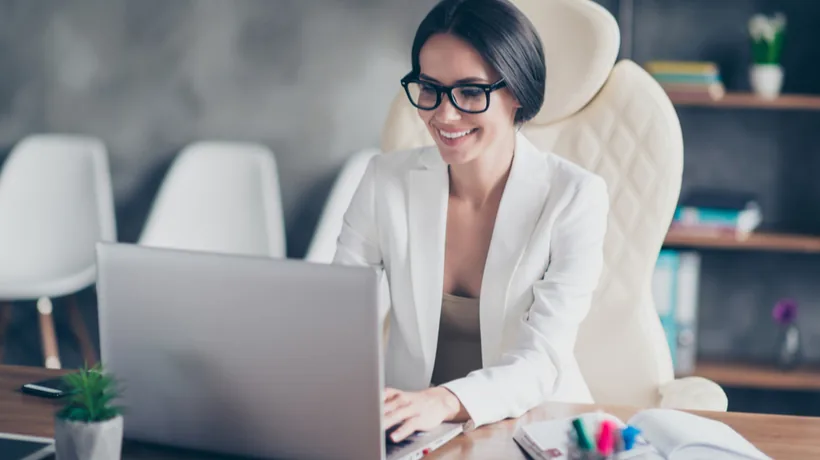 Donna sorridente lavora al computer in ufficio moderno, rappresentando l’esperienza utente positiva su una piattaforma LMS